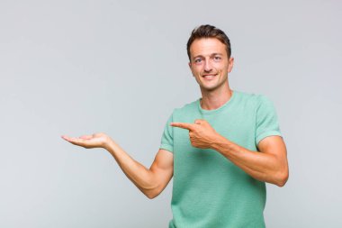 Genç yakışıklı adam gülümsüyor, mutlu, tasasız ve tatmin olmuş hissediyor, fotokopi alanındaki konsepte ya da fikre işaret ediyor.