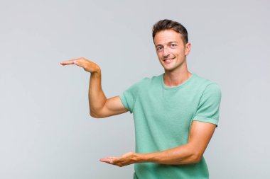 Genç yakışıklı adam gülümsüyor, mutlu, pozitif ve tatmin olmuş hissediyor, fotokopi alanında nesne ya da konsept tutuyor ya da gösteriyor