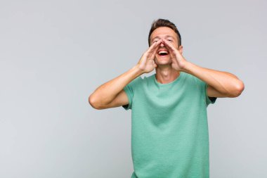 Genç yakışıklı adam mutlu, heyecanlı ve pozitif hissediyor. Elleri ağızda, bağırıyor.