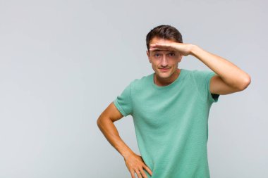 Genç yakışıklı adam şaşkın ve şaşkın bakıyor, el üstünde uzak bakıyor, izliyor ya da arıyor