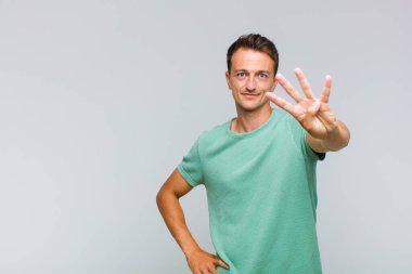 Genç yakışıklı adam gülümsüyor ve arkadaş canlısı görünüyor, 4 ya da 4 numarayı gösteriyor, eli önde, geri sayıyor.