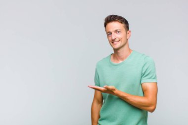 Genç yakışıklı adam neşeyle gülümsüyor, mutlu hissediyor ve fotokopi uzayında bir konsept gösteriyor.