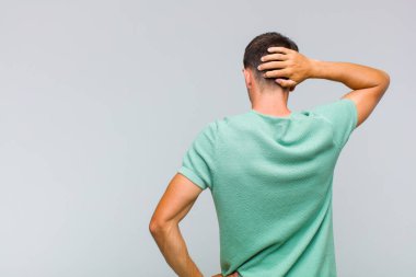 Genç yakışıklı adam düşünüyor ya da şüphe ediyor, kafasını kaşıyor, şaşkın ve kafası karışık hissediyor, arkaya ya da arkaya bakıyor.