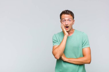 Genç yakışıklı adam şok ve inançsızlık içinde, elleri yanak ve kolları çapraz, sersemlemiş ve şaşırmış hissediyor.