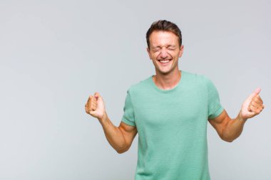 Genç yakışıklı adam çok mutlu ve şaşırmış görünüyor, başarıyı kutluyor, bağırıyor ve zıplıyor.