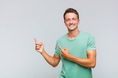 Genç yakışıklı adam mutlu bir şekilde gülümsüyor ve her iki elinde fotokopi alanında nesne gösteriyor.