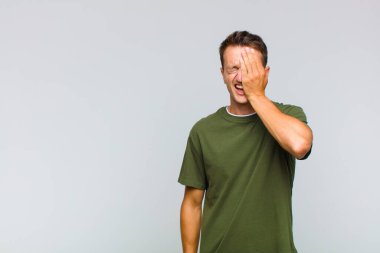 Genç yakışıklı adam uykulu, sıkılmış ve esniyor, baş ağrısı ve yüzünün yarısını kaplayan bir elle.