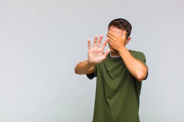 Genç ve yakışıklı bir adam elleriyle yüzünü kapatıyor ve kamerayı durdurmak için diğer elini öne koyuyor. Fotoğraf ya da resimleri reddediyor.