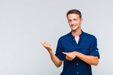 Genç yakışıklı adam neşeyle gülümsüyor ve yan taraftaki fotokopi alanını gösteriyor, mutlu ve tatmin olmuş hissediyor.