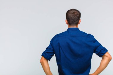 Genç, yakışıklı bir adam kafası karışık ya da dolu ya da şüphe ve soru dolu, merak ediyor, elleri kalçasında, dikiz aynasından.