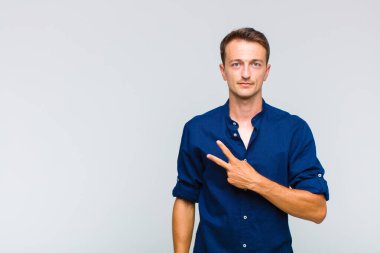 Genç yakışıklı adam kendini mutlu, pozitif ve başarılı hissediyor. Göğsünde el ile V şekli yapıyor. Zafer ya da huzur gösteriyor.