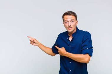 Genç yakışıklı adam şaşkın ve şaşırmış hissediyor. Kenardaki fotokopi alanını işaret ediyor. Şaşırmış, ağzı açık bir bakış.