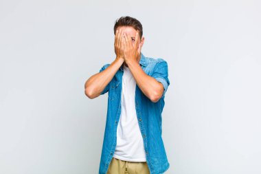 Genç yakışıklı adam elleriyle yüzünü kapatıyor, parmaklarının arasından şaşkın bir ifadeyle yan tarafa bakıyor.