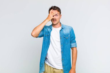 Genç yakışıklı adam şok olmuş, korkmuş ya da korkmuş görünüyor. Yüzü elle kaplanmış ve parmaklarının arasından gizlice bakıyor.
