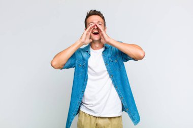 Genç yakışıklı adam mutlu, heyecanlı ve pozitif hissediyor. Elleri ağızda, bağırıyor.