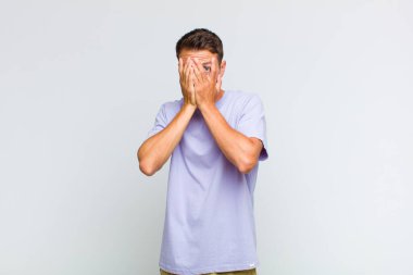 Genç ve yakışıklı bir adam korkmuş ya da utanmış hissediyor. Gözleri yarı kapalı ya da ellerle dikizliyor ya da dikizliyor.