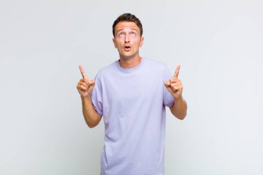 Genç ve yakışıklı bir adam şaşkınlık ve şaşkınlık dolu bakışlarla yukarıyı işaret ederek huşu içinde ve açık ağızlı hissediyor.