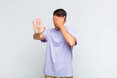 Genç ve yakışıklı bir adam elleriyle yüzünü kapatıyor ve kamerayı durdurmak için diğer elini öne koyuyor. Fotoğraf ya da resimleri reddediyor.