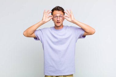 Genç yakışıklı adam şaşkın, şaşırmış ve şaşırmış hissediyor. Elinde şaşkın, inançsız bir bakışla gözlük tutuyor.