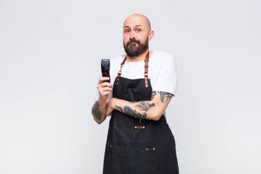 Kel adam omuz silkiyor, kafası karışık ve kararsız, kolları bağlı ve şaşkın bir şekilde şüpheye düşmüş görünüyor.