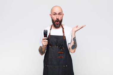 Kel adam şaşırmış ve şoka uğramış görünüyor, çenesi düşmüş ve eli açık bir nesneyi tutuyor.