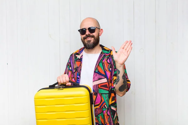 bald man smiling happily and cheerfully, waving hand, welcoming and greeting you, or saying goodbye