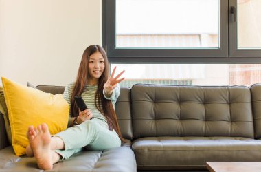 Genç Asyalı kadın gülümsüyor ve arkadaş canlısı görünüyor, üç ya da üç numarayı gösteriyor, eli önde, geriye doğru sayıyor.