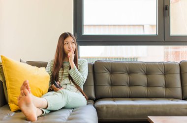 Genç Asyalı kadın düşünüyor, kuşkulu ve şaşkın hissediyor, farklı seçeneklerle, hangi kararı vereceğini merak ediyor.