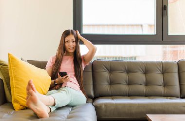 Asyalı genç bir kadın kendini stresli, endişeli, endişeli ya da korkmuş hissediyor. Elleri başının üstünde, hatayla panikliyor.