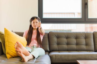 Asyalı genç bir kadın kızgın, sinirli, hayal kırıklığına uğramış ya da canı sıkkın, ciddi bir bakışla başparmağını kaldırıyor.