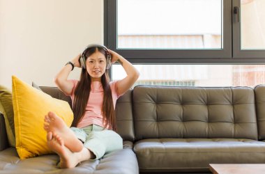 Asyalı genç bir kadın kendini stresli, endişeli, endişeli ya da korkmuş hissediyor. Elleri başının üstünde, hatayla panikliyor.