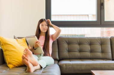 Genç Asyalı kadın şaşkın ve kafası karışmış hissediyor, başını kaşıyor ve yan tarafa bakıyor.