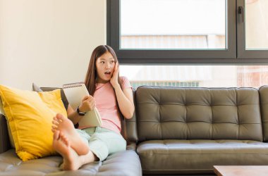 Asyalı genç bir kadın mutlu, heyecanlı ve şaşırmış hissediyor, iki eli yüzü yana bakıyor.