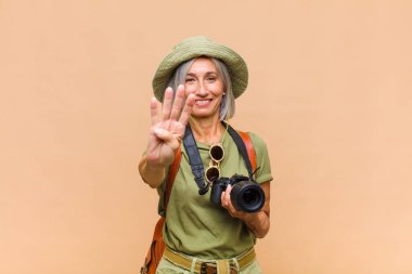 Orta yaşlı bir kadın gülümsüyor ve arkadaş canlısı görünüyor. Elleri önde, geriye doğru sayıyor.