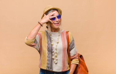 Orta yaşlı bir kadın şok olmuş, korkmuş ya da korkmuş görünüyor. Yüzü elle kaplanmış ve parmaklarının arasından gizlice bakıyor.