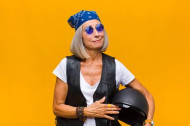 Orta yaşlı bir kadın omuz silkiyor, kafası karışık ve kararsız, kolları bağlı ve şaşkın görünüyor.