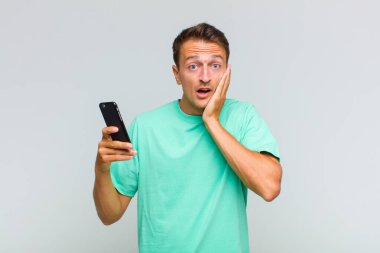 Genç yakışıklı adam şok olmuş ve korkmuş hissediyor, ağzı açık ve elleri yanaklarında korkmuş görünüyor.