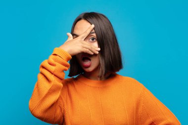 İspanyol kadın şok olmuş, korkmuş ya da korkmuş görünüyor. Yüzü elle kaplanmış ve parmaklarının arasından gizlice bakıyor.