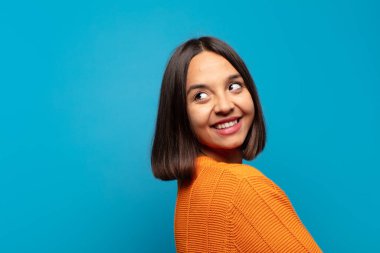 İspanyol kadın neşeyle gülümsüyor, mutlu, tatmin olmuş ve rahatlamış hissediyor, kollarını kavuşturup yan tarafa bakıyor.