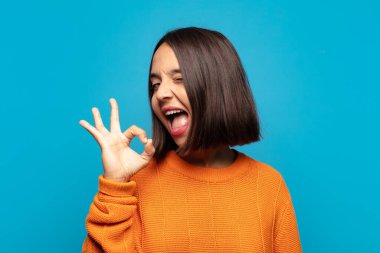 İspanyol kadın kendini başarılı ve tatmin olmuş hissediyor, ağzı açık gülümsüyor, elle işaret veriyor.