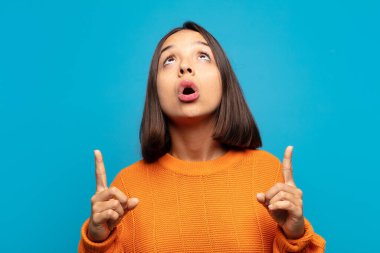 Hispanik kadın şaşkınlık içinde ve ağzı açık. Şok olmuş ve şaşırmış bir bakışla yukarı bakıyor.