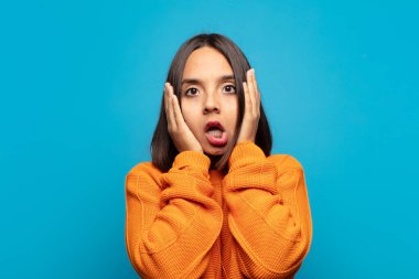 İspanyol kadın hoş olmayan bir şekilde şok olmuş, korkmuş ya da endişeli görünüyor, ağzı sonuna kadar açık ve iki kulağını da elleriyle kapatıyor.