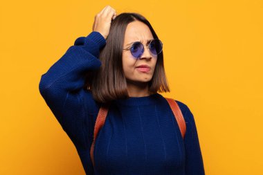 İspanyol kadın şaşkın ve şaşkın hissediyor, kafasını kaşıyor ve yan tarafa bakıyor.