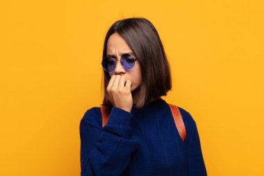 Hispanik kadın ciddi, düşünceli ve endişeli, elleri çenesine bastırılmış bir şekilde yan bakıyor