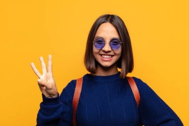 İspanyol kadın gülümsüyor ve arkadaş canlısı görünüyor. Üç ya da üç numarayı gösteriyor. Elleri önde, geri sayıyor.