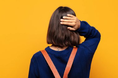 Hispanik kadın düşünüyor ya da şüphe ediyor, kafasını kaşıyor, şaşkın ve şaşkın hissediyor, arkaya ya da arkaya bakıyor.