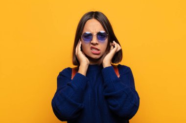 İspanyol kadın sinirli, stresli ve sinirli görünüyor, iki kulağını da sağır edici bir ses, ses ya da yüksek sesle kapatıyor.