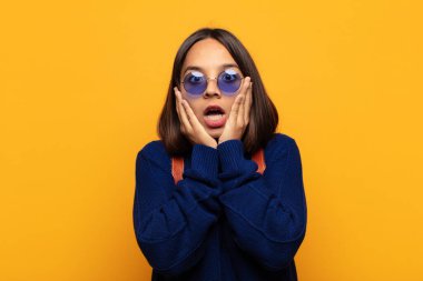 İspanyol kadın şok olmuş ve korkmuş hissediyor, ağzı açık ve elleri yanaklarında korkmuş görünüyor.