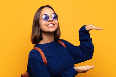 İspanyol bir kadın, iki eli yanda olan bir objeyi tutuyor fotokopi alanında, bir nesneyi gösteriyor, sunuyor ya da reklamını yapıyor.