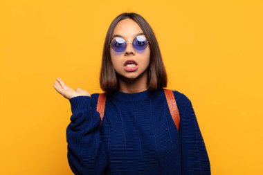 İspanyol kadın şaşırmış ve şoka uğramış görünüyor, çenesi düşmüş, eli açık bir objeyi tutuyor.